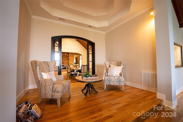 living area with wood-type flooring, a tray ceiling, and crown molding