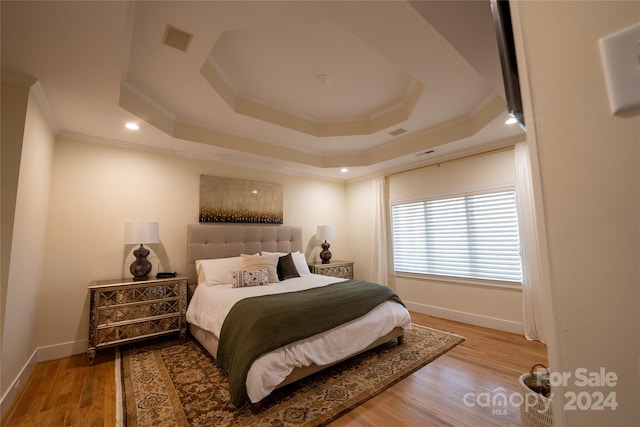 bedroom with light hardwood / wood-style flooring, a raised ceiling, and ornamental molding