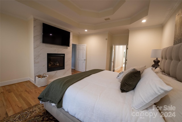 bedroom featuring wood-type flooring, a raised ceiling, ornamental molding, and a high end fireplace