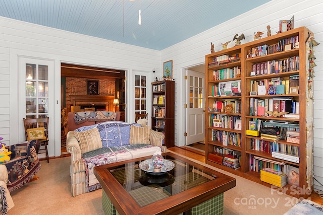 living room featuring light carpet, a fireplace, and wood walls