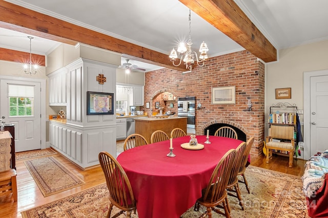 dining space featuring crown molding, a fireplace, light wood-type flooring, ceiling fan with notable chandelier, and beamed ceiling