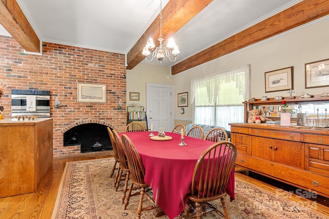 dining room featuring brick wall, light hardwood / wood-style flooring, beamed ceiling, a brick fireplace, and a notable chandelier