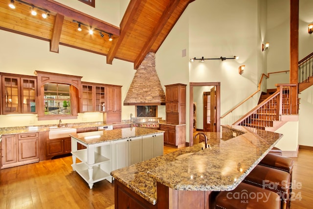 kitchen with a large island with sink, sink, light wood-type flooring, wooden ceiling, and high vaulted ceiling