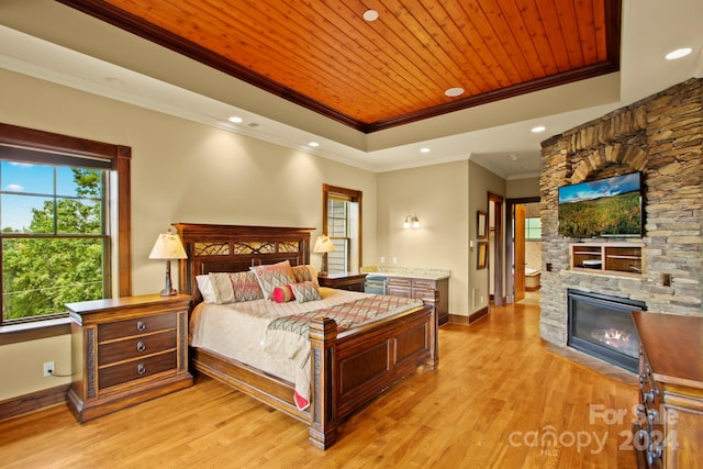 bedroom featuring a stone fireplace, a tray ceiling, wooden ceiling, ornamental molding, and light hardwood / wood-style floors