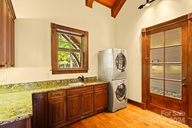 clothes washing area with light hardwood / wood-style flooring, stacked washing maching and dryer, cabinets, and sink