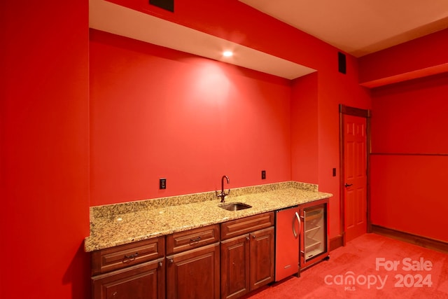 kitchen with sink, light stone counters, light colored carpet, and beverage cooler