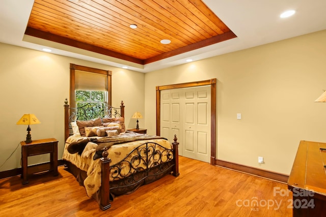 bedroom featuring light hardwood / wood-style flooring, a tray ceiling, a closet, and wooden ceiling