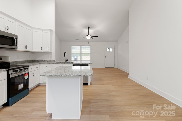 kitchen featuring sink, appliances with stainless steel finishes, white cabinetry, a center island, and light stone counters