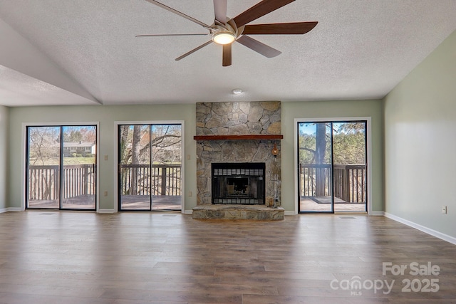 unfurnished living room featuring a textured ceiling, a ceiling fan, wood finished floors, and a stone fireplace