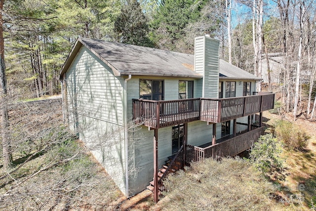 back of house with a deck, a shingled roof, and a chimney