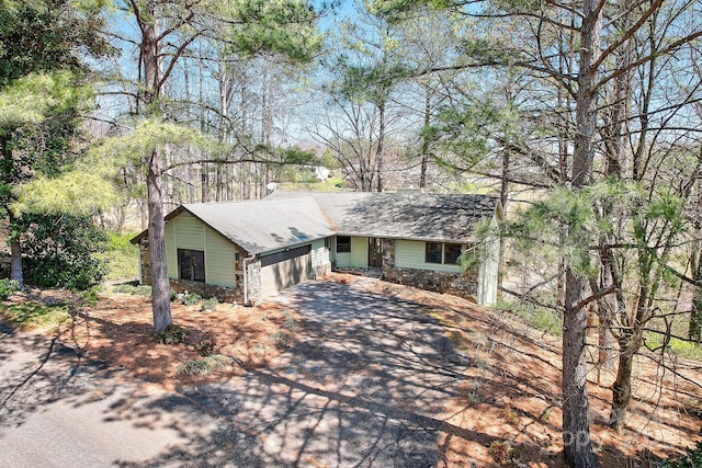 view of front facade featuring a garage, stone siding, aphalt driveway, and roof with shingles