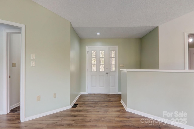 foyer entrance with a textured ceiling, wood finished floors, visible vents, and baseboards