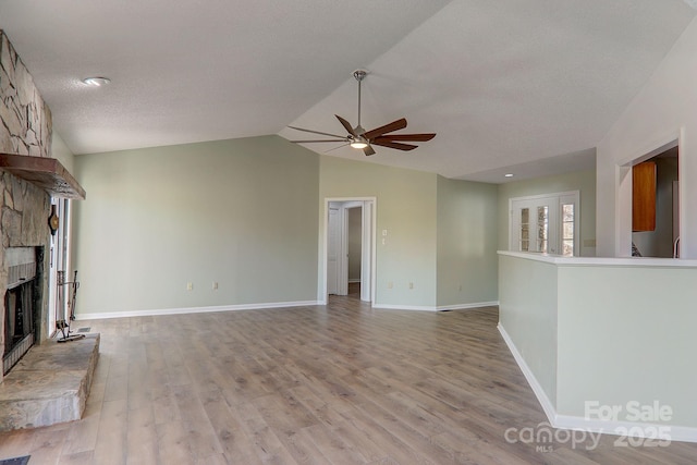 unfurnished living room with light wood finished floors, lofted ceiling, a ceiling fan, a stone fireplace, and baseboards