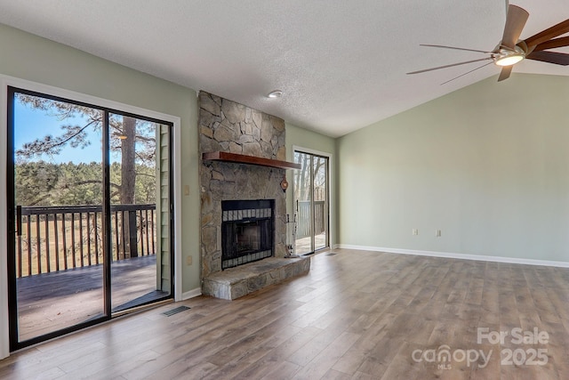 unfurnished living room with a healthy amount of sunlight, vaulted ceiling, a stone fireplace, and wood finished floors