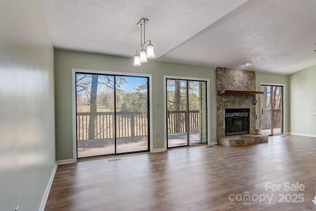 unfurnished living room featuring visible vents, a healthy amount of sunlight, a stone fireplace, and wood finished floors