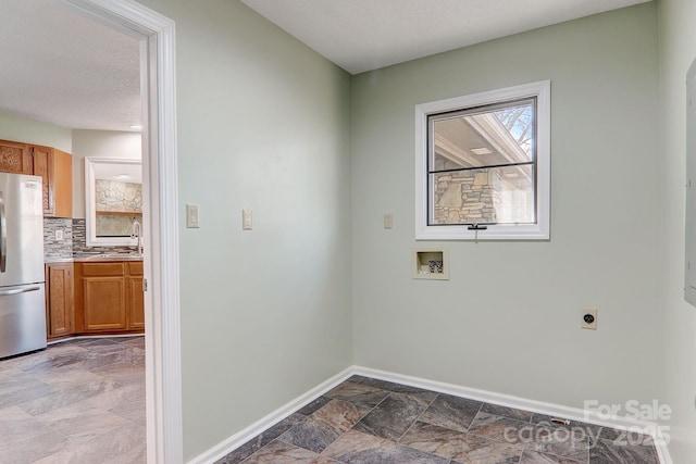 laundry room featuring hookup for a washing machine, stone finish floor, a sink, electric dryer hookup, and baseboards