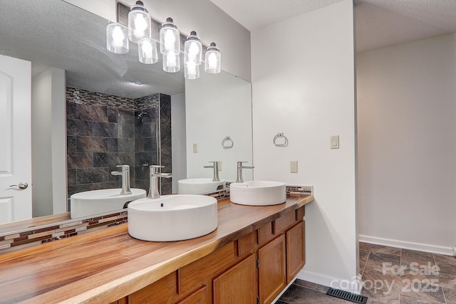 bathroom featuring tiled shower, a sink, and visible vents