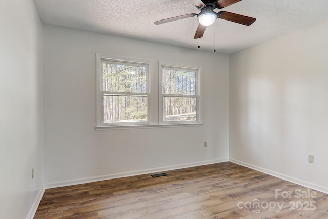 spare room with a textured ceiling, wood finished floors, visible vents, and baseboards