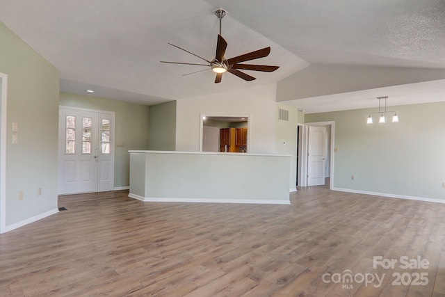 unfurnished living room featuring baseboards, visible vents, lofted ceiling, wood finished floors, and ceiling fan with notable chandelier