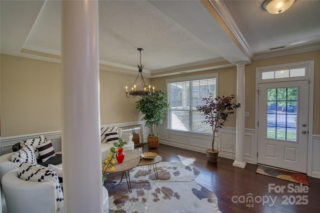 entrance foyer with dark hardwood / wood-style floors, crown molding, a chandelier, and decorative columns