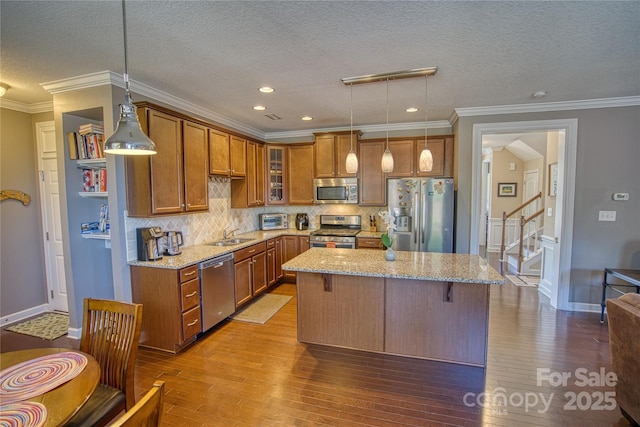 kitchen featuring appliances with stainless steel finishes, a center island, decorative light fixtures, and light stone counters