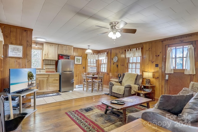 living room with wood walls, ceiling fan, light wood-type flooring, and a baseboard heating unit