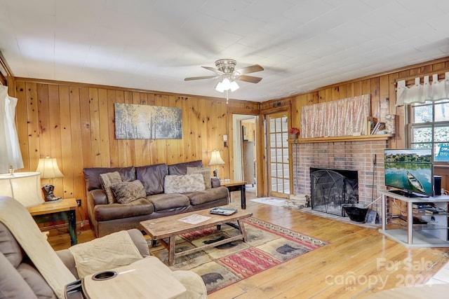 living room with wood walls, a brick fireplace, ceiling fan, and hardwood / wood-style floors