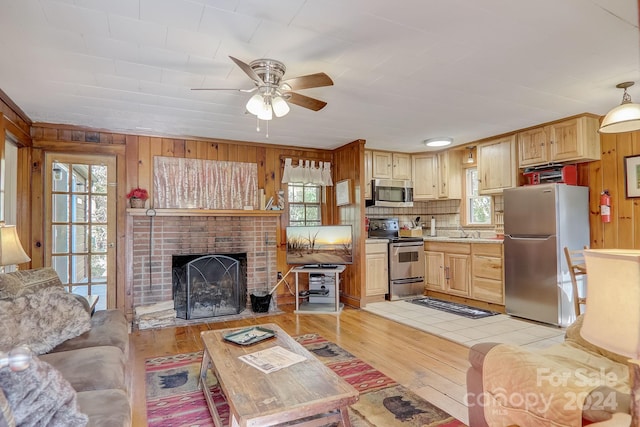 living room featuring a brick fireplace, ceiling fan, wooden walls, sink, and light wood-type flooring