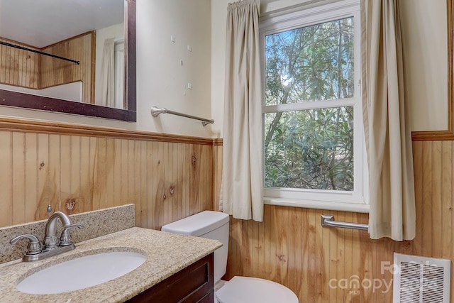 bathroom with wood walls, toilet, and vanity