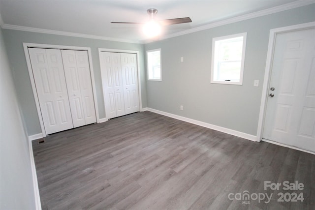 unfurnished bedroom featuring ceiling fan, two closets, wood-type flooring, and crown molding