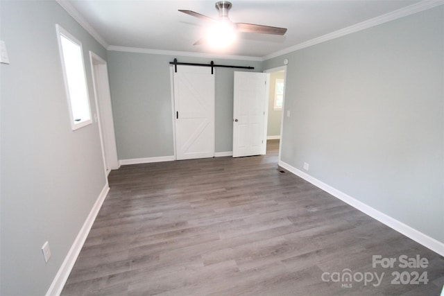 unfurnished bedroom featuring ceiling fan, wood-type flooring, crown molding, and a barn door