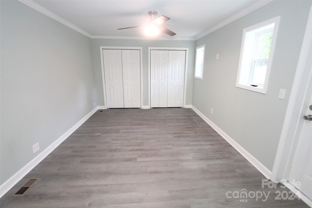 unfurnished bedroom featuring ceiling fan, wood-type flooring, ornamental molding, and multiple closets