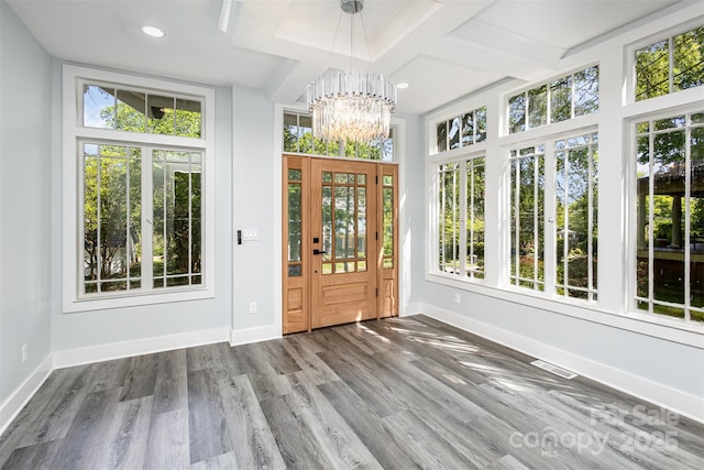 unfurnished sunroom featuring beamed ceiling, a notable chandelier, plenty of natural light, and coffered ceiling