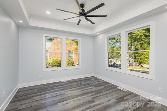 empty room with ceiling fan, dark hardwood / wood-style flooring, ornamental molding, and a tray ceiling