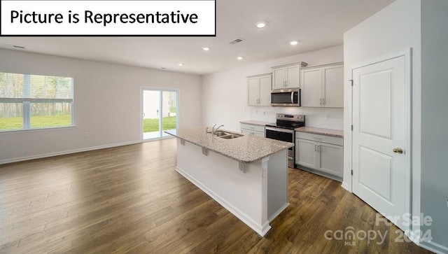 kitchen featuring an island with sink, light stone counters, dark wood-type flooring, and stainless steel appliances