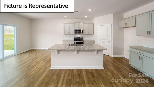 kitchen featuring light stone counters, an island with sink, appliances with stainless steel finishes, and dark hardwood / wood-style floors