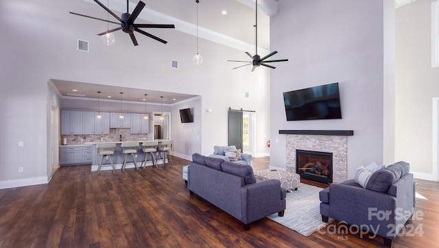 living room with a barn door, ceiling fan, dark hardwood / wood-style flooring, a towering ceiling, and a fireplace