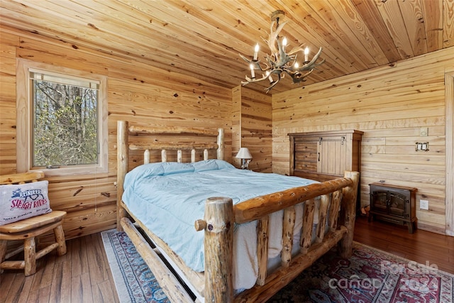 bedroom with a wood stove, an inviting chandelier, wooden ceiling, and hardwood / wood-style floors