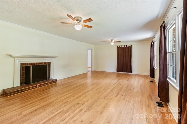 unfurnished living room with ceiling fan, a fireplace, a textured ceiling, and light wood-type flooring