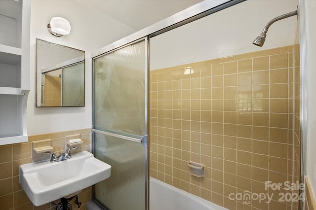 bathroom featuring tasteful backsplash, combined bath / shower with glass door, tile walls, and sink