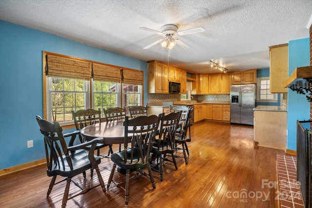 dining room with a textured ceiling, ceiling fan, hardwood / wood-style flooring, and track lighting