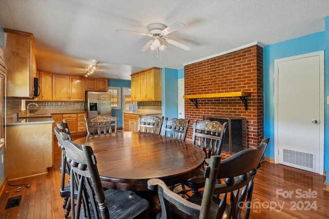 dining area with a textured ceiling, a brick fireplace, ceiling fan, and hardwood / wood-style floors