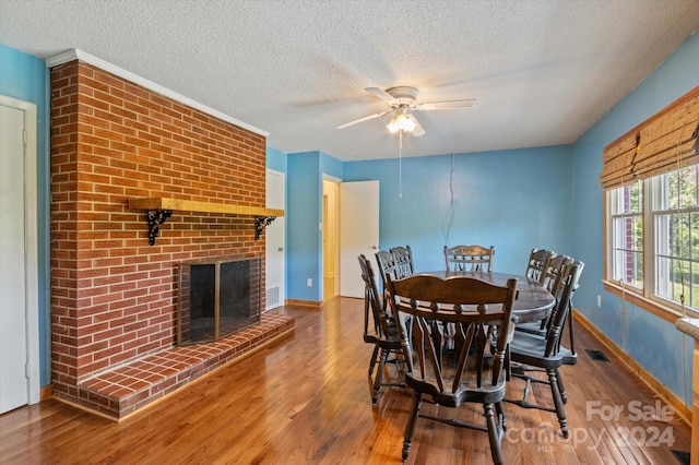 dining space featuring a textured ceiling, ceiling fan, hardwood / wood-style floors, and a fireplace