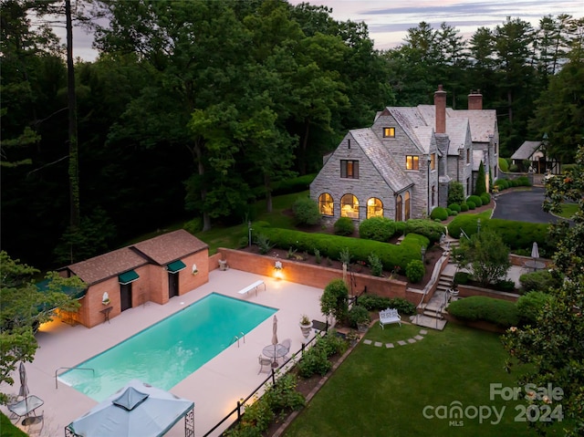 pool at dusk with a patio, a diving board, and an outdoor structure