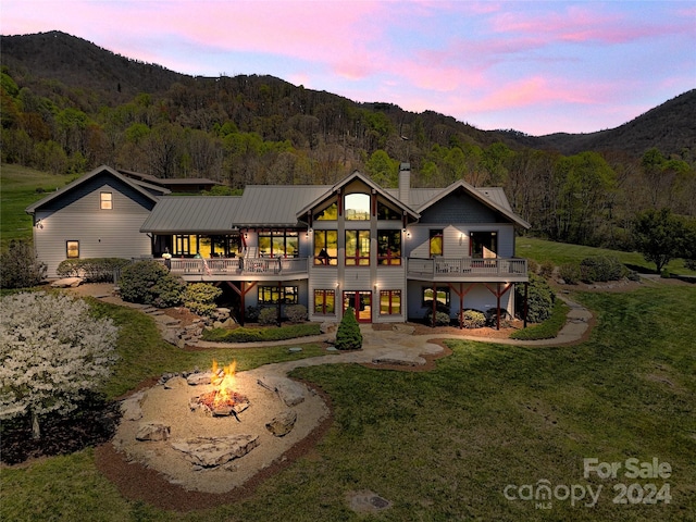 back house at dusk featuring a deck with mountain view, a lawn, and a fire pit