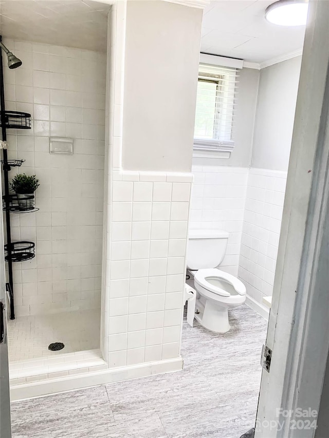 bathroom featuring crown molding, toilet, tiled shower, and tile walls