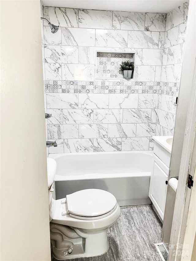 full bathroom featuring wood-type flooring, vanity, tiled shower / bath combo, and toilet