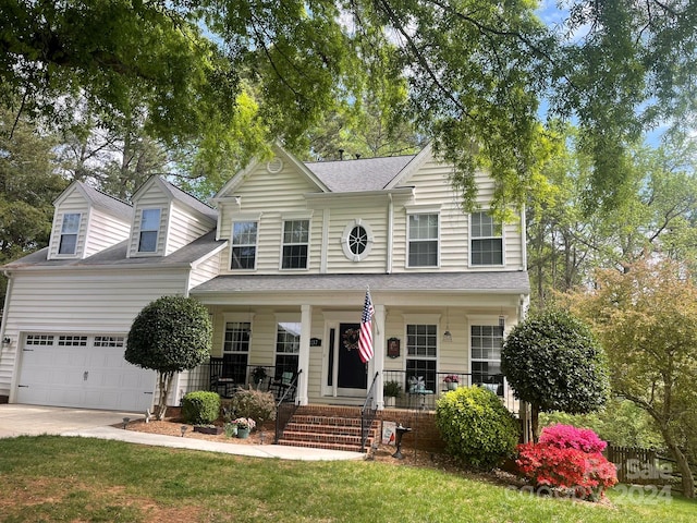 view of front of house with driveway, roof with shingles, a porch, an attached garage, and a front lawn