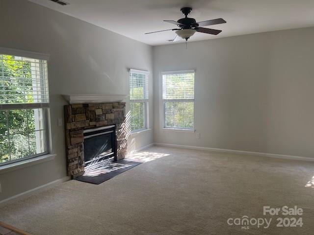 unfurnished living room with carpet flooring, ceiling fan, and a stone fireplace