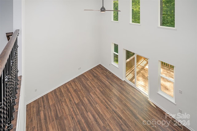 unfurnished living room featuring a wealth of natural light, dark wood-type flooring, ceiling fan, and a towering ceiling